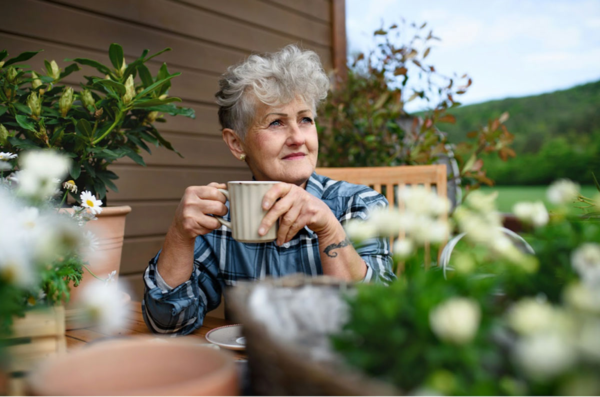 Senior woman sitting on a patio holding a mug.